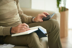 Pessoa sentada no sofá fazendo cálculos com calculadora e caderno 